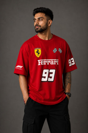 Close-up of a red Ferrari oversized t-shirt featuring the iconic yellow prancing horse logo and 'Ferrari 93' graphic. The fabric has a premium, textured look, showcasing high-quality print and material.