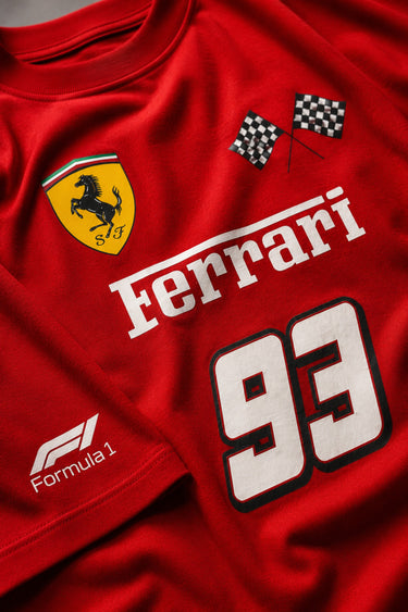 Close-up of a red Ferrari oversized t-shirt featuring the iconic yellow prancing horse logo and 'Ferrari 93' graphic. The fabric has a premium, textured look, showcasing high-quality print and material.