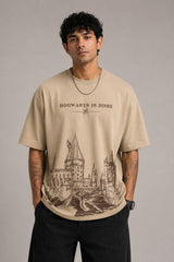 Beige oversized t-shirt with "Hogwarts is Home" text and a detailed sketch of Hogwarts castle. Premium cotton fabric visible.