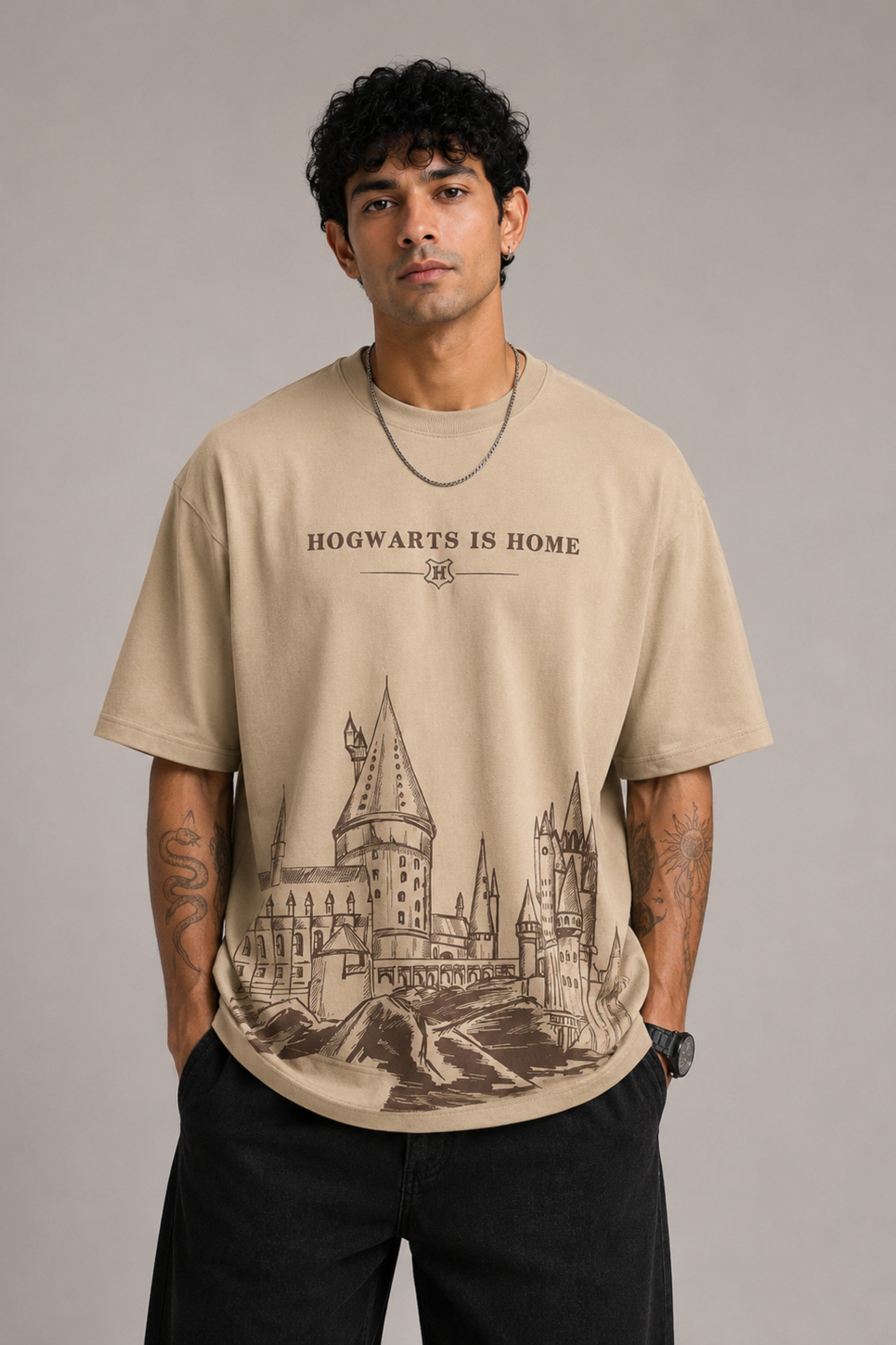 Beige oversized t-shirt with "Hogwarts is Home" text and a detailed sketch of Hogwarts castle. Premium cotton fabric visible.
