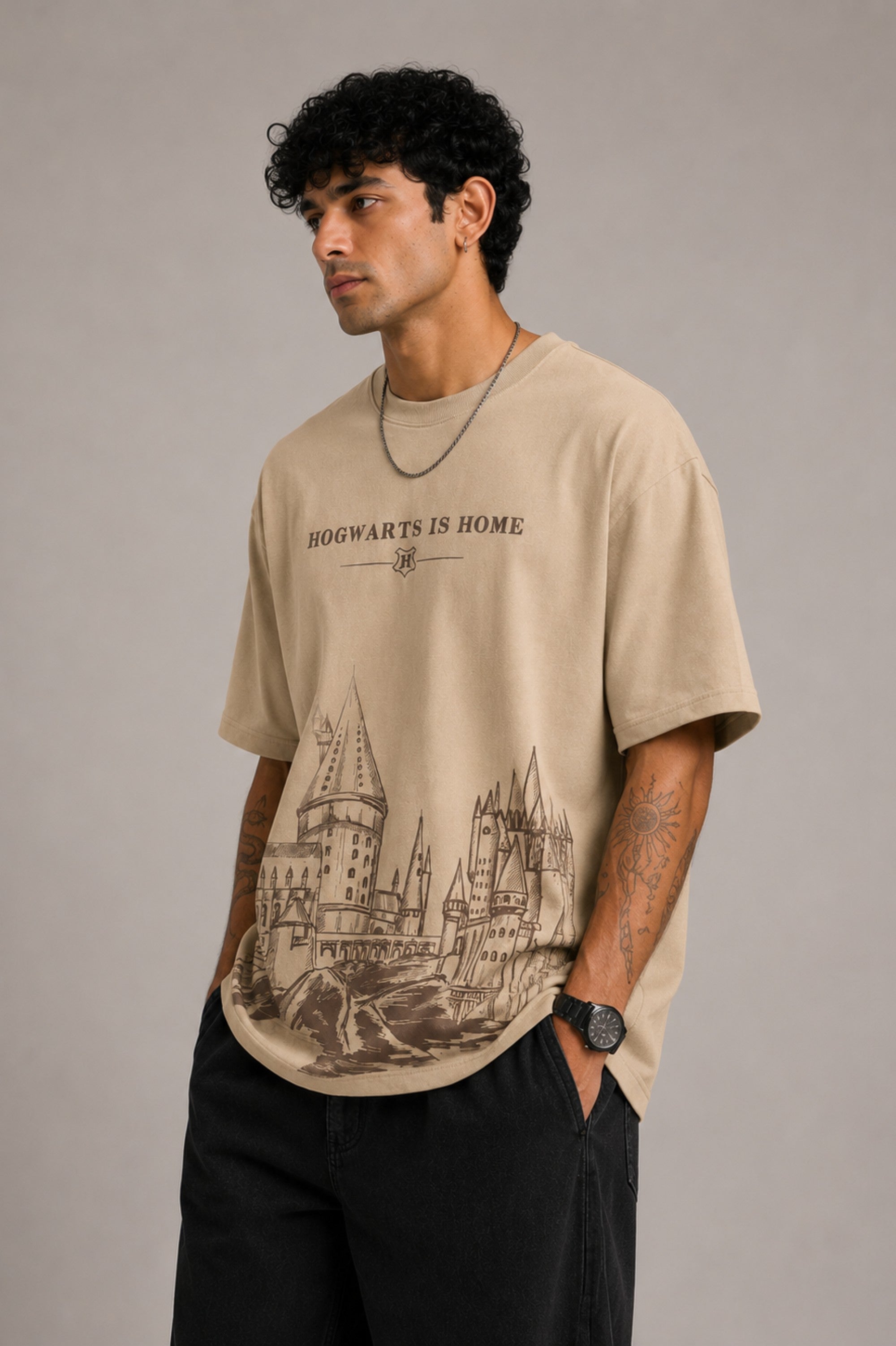 Beige oversized t-shirt with "Hogwarts is Home" text and a detailed sketch of Hogwarts castle. Premium cotton fabric visible.