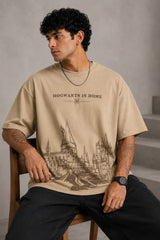 Beige oversized t-shirt with "Hogwarts is Home" text and a detailed sketch of Hogwarts castle. Premium cotton fabric visible.