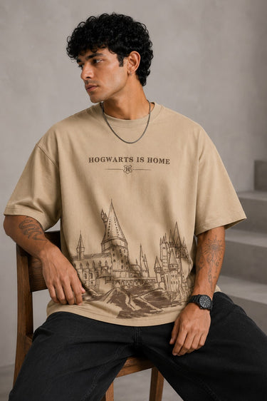 Beige oversized t-shirt with "Hogwarts is Home" text and a detailed sketch of Hogwarts castle. Premium cotton fabric visible.