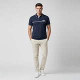 Man wearing a navy polo shirt with a logo and beige pants on a light gray background