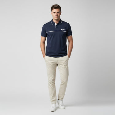 Man wearing a navy polo shirt with a logo and beige pants on a light gray background