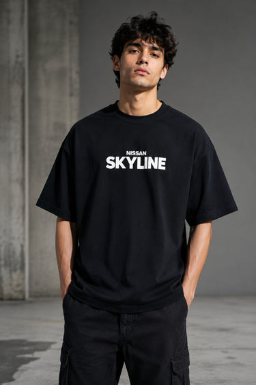 Black oversized t-shirt featuring a detailed white blueprint and a silver Nissan Skyline R34 with blue racing stripes graphic. Includes text 'The Nissan Skyline GTR'.
