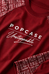 Dark red POPCASE 'Unstoppable' oversized t-shirt with white raised print, featuring ethnic patterned sleeves. Close-up shot showcasing fabric texture and print detail.