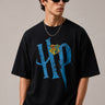 Model wearing a black Harry Potter Gryffindor oversized t-shirt with a blue 'HP' graphic and Hogwarts crest. Features black sunglasses, silver necklace, and dark pants. - black