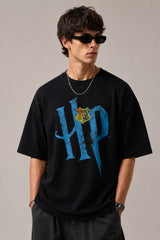 Model wearing a black Harry Potter Gryffindor oversized t-shirt with a blue 'HP' graphic and Hogwarts crest. Features black sunglasses, silver necklace, and dark pants. - black