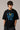 Model wearing a black Harry Potter Gryffindor oversized t-shirt with a blue 'HP' graphic and Hogwarts crest. Features black sunglasses, silver necklace, and dark pants. - black