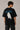 Model wearing a black Harry Potter Gryffindor oversized t-shirt with a blue 'HP' graphic and Hogwarts crest. Features black sunglasses, silver necklace, and dark pants.