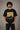 Back view of a man wearing an ENFIELD DESIGN black oversized t-shirt against a textured grey background. Features relaxed fit and premium cotton. - black