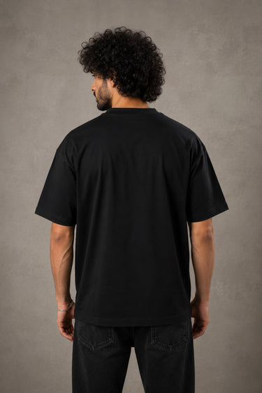 Back view of a man wearing an ENFIELD DESIGN black oversized t-shirt against a textured grey background. Features relaxed fit and premium cotton. - 2