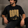 Back view of a man wearing an ENFIELD DESIGN black oversized t-shirt against a textured grey background. Features relaxed fit and premium cotton. - 3