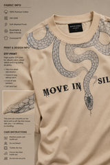 Beige oversized t-shirt with a detailed vintage-style grey snake graphic and 'MOVE IN SILENCE' text. The fabric is soft-washed premium cotton.