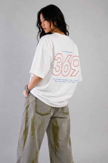 White oversized t-shirt from The Six Design featuring a bold red and blue graphic print of the numbers 3, 6, and 9. The t-shirt has a relaxed fit and is made of premium cotton.
