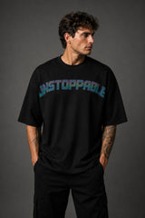 Man wearing a black UNSTOPPABLE DESIGN oversized t-shirt with a vibrant, detailed graphic of a roaring tiger surrounded by red flowers and a geometric frame on the back.