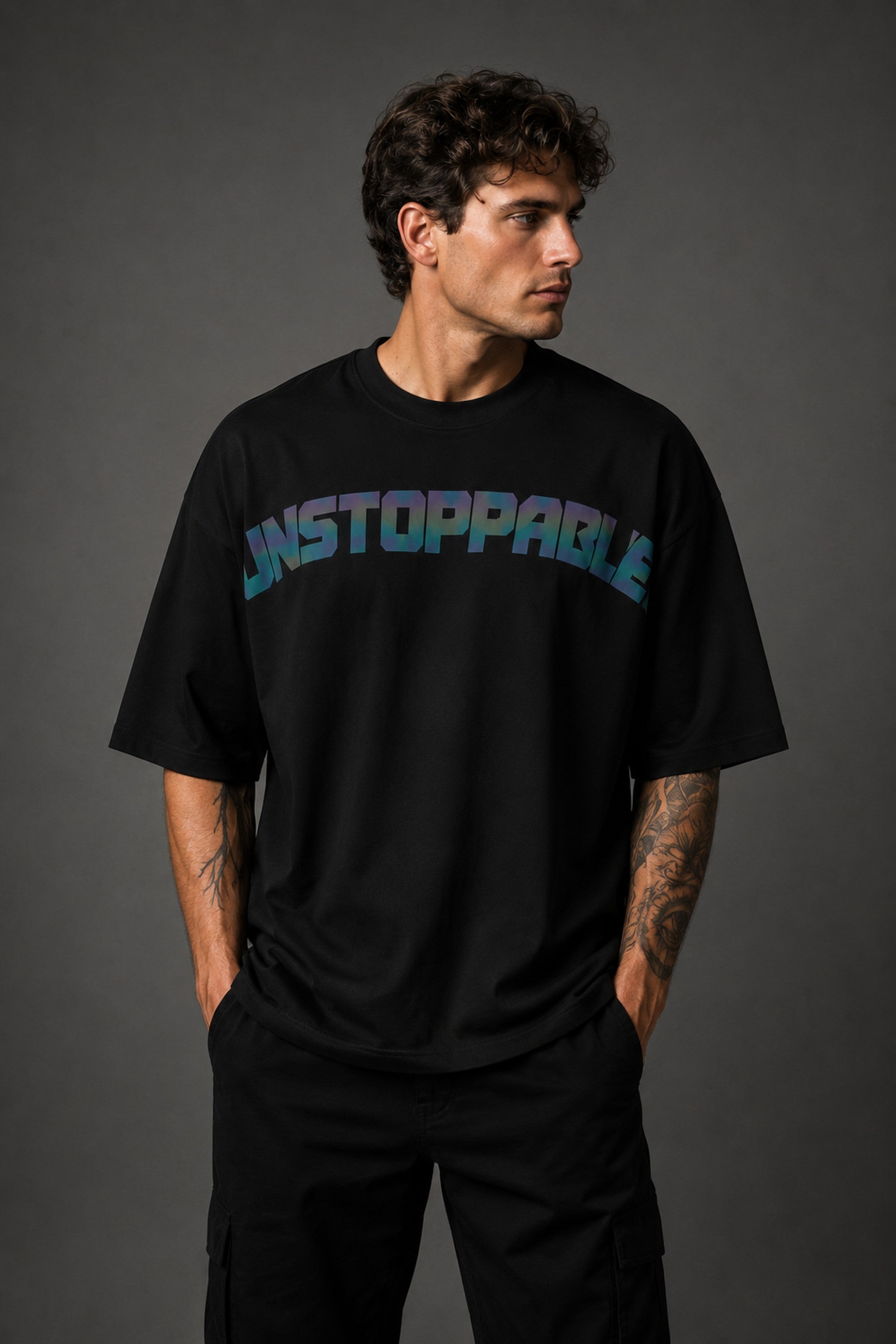 Man wearing a black UNSTOPPABLE DESIGN oversized t-shirt with a vibrant, detailed graphic of a roaring tiger surrounded by red flowers and a geometric frame on the back.