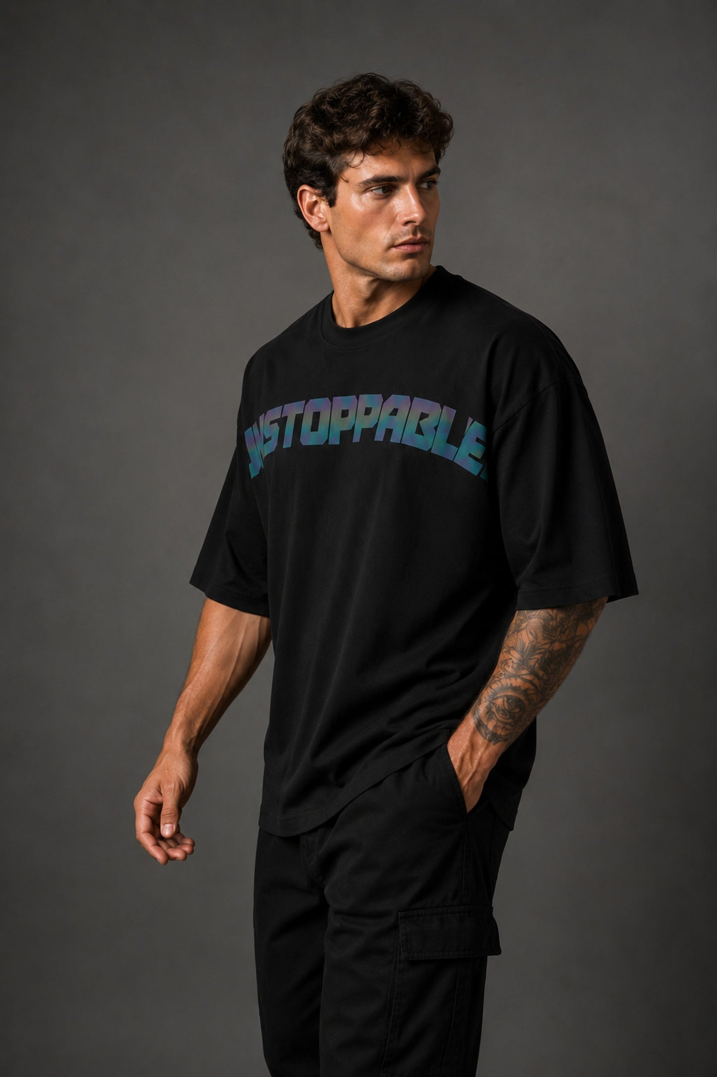 Man wearing a black UNSTOPPABLE DESIGN oversized t-shirt with a vibrant, detailed graphic of a roaring tiger surrounded by red flowers and a geometric frame on the back.