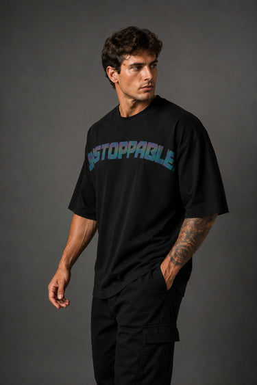 Man wearing a black UNSTOPPABLE DESIGN oversized t-shirt with a vibrant, detailed graphic of a roaring tiger surrounded by red flowers and a geometric frame on the back.
