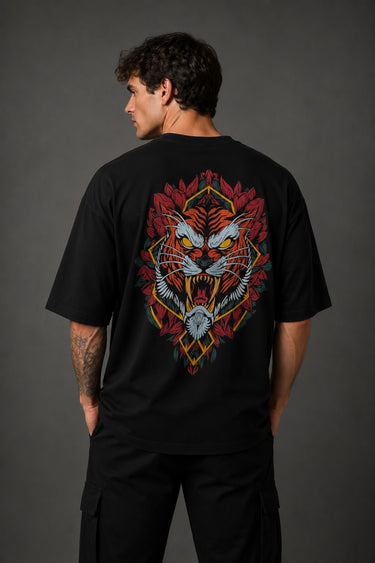 Man wearing a black UNSTOPPABLE DESIGN oversized t-shirt with a vibrant, detailed graphic of a roaring tiger surrounded by red flowers and a geometric frame on the back.