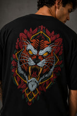 Man wearing a black UNSTOPPABLE DESIGN oversized t-shirt with a vibrant, detailed graphic of a roaring tiger surrounded by red flowers and a geometric frame on the back.