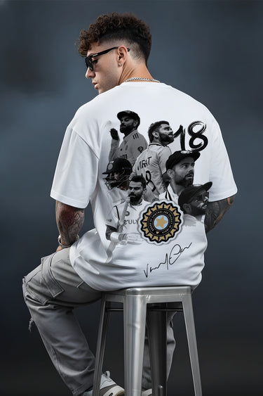 Person wearing a white t-shirt with graphic designs and text, sitting on a stool against a dark background.